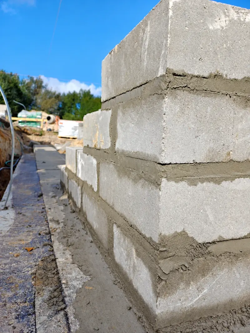 Narożnik ściany fundamentowej z bloczków betonowych na zaprawie, pierwsze warstwy na zaizolowanej ławie – budowa domu Kordian STO w Grabinie, październik 2026